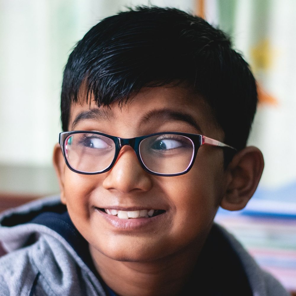 A boy in glasses, smiling and looking to one side