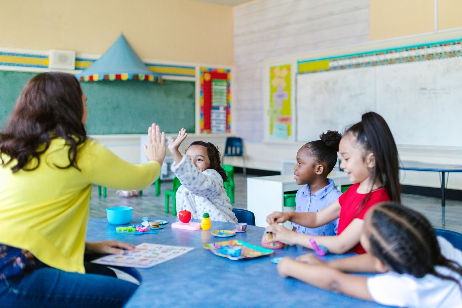 A teacher high-fiving a girl at a classroom table