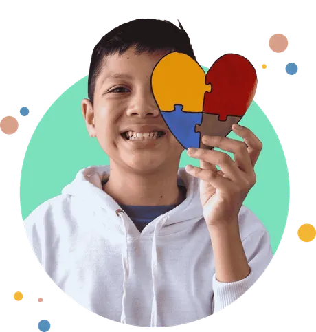 A smiling boy holds a colourful puzzle-piece heart over one eye