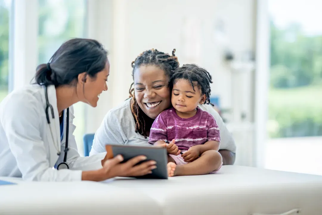 A doctor showing a tablet to a smiling mother who is holding her toddler