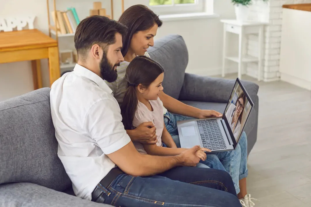 Two parents and their daughter on a sofa, looking at a laptop together
