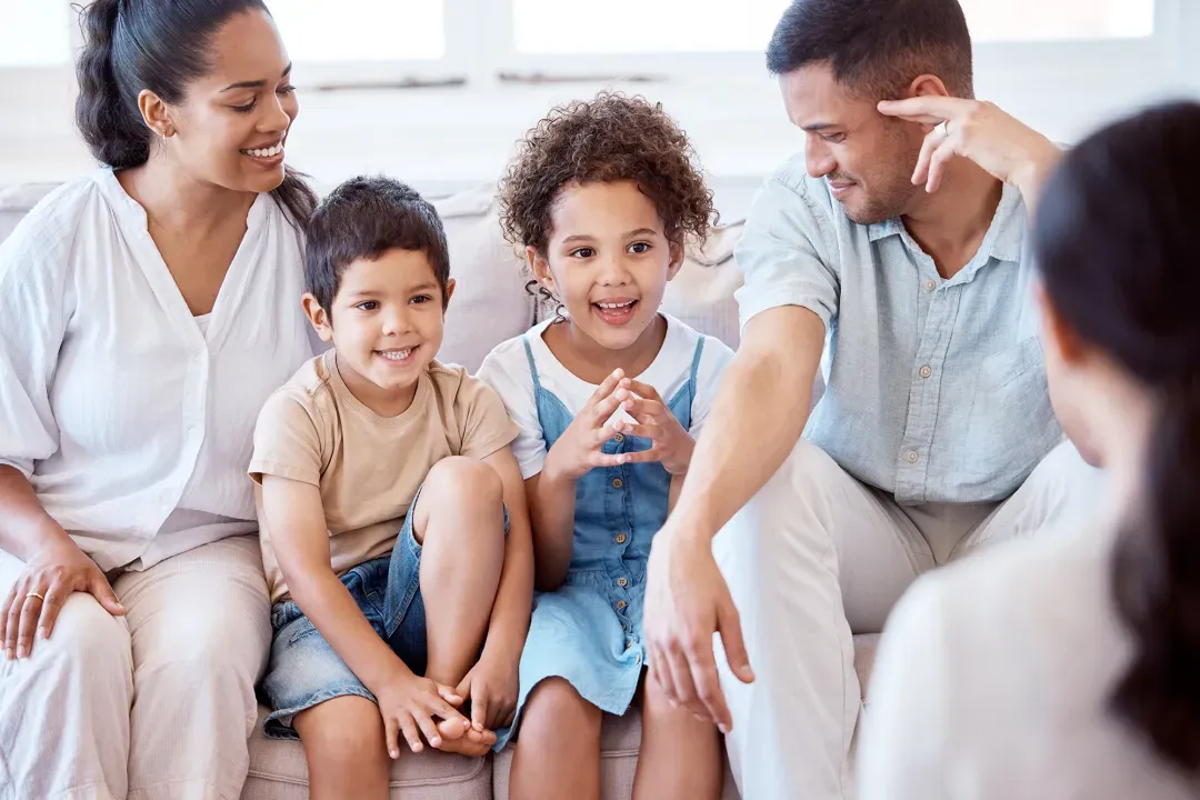 Two parents on a sofa with their son and daughter, smiling at a clinician