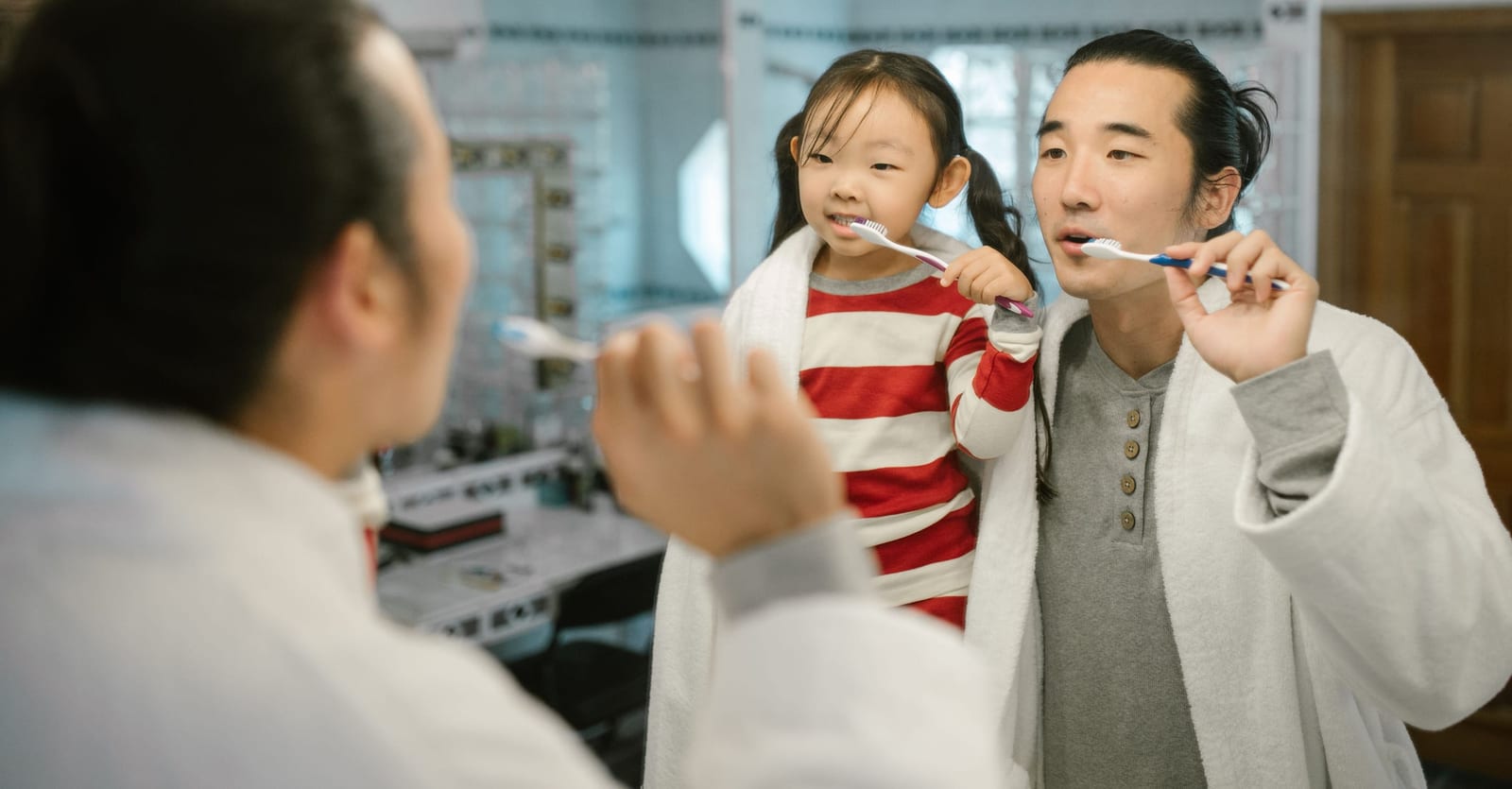 A father and his young daughter brushing their teeth side by side